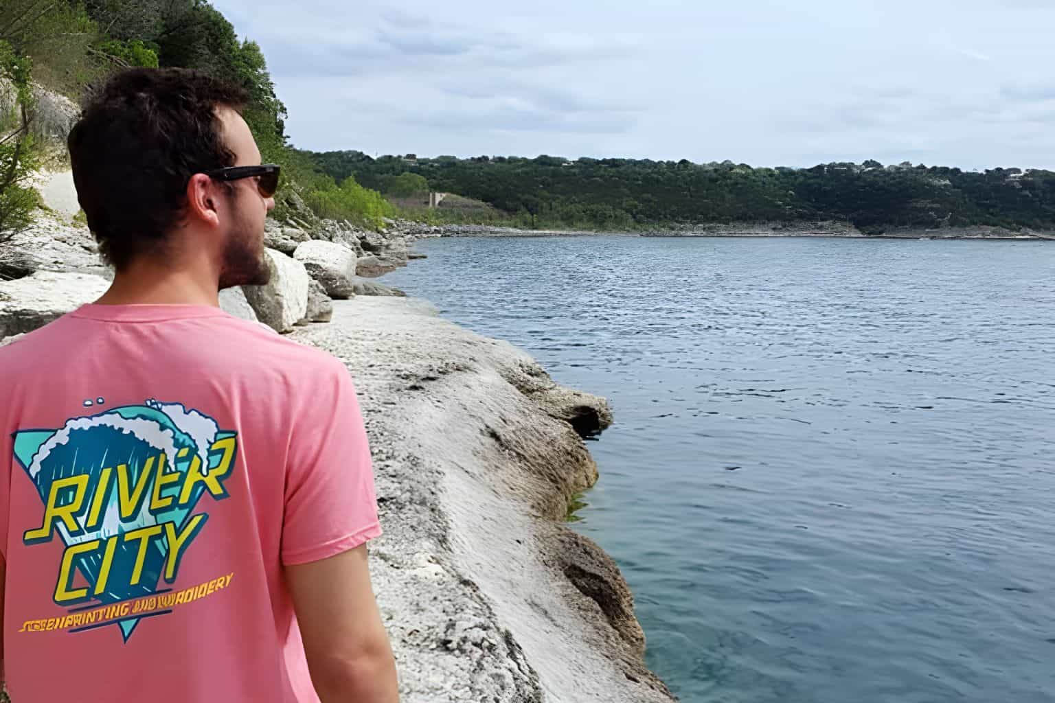 A man wearing a t-shirt with a multi-colored screen printed design, looking out over the water.